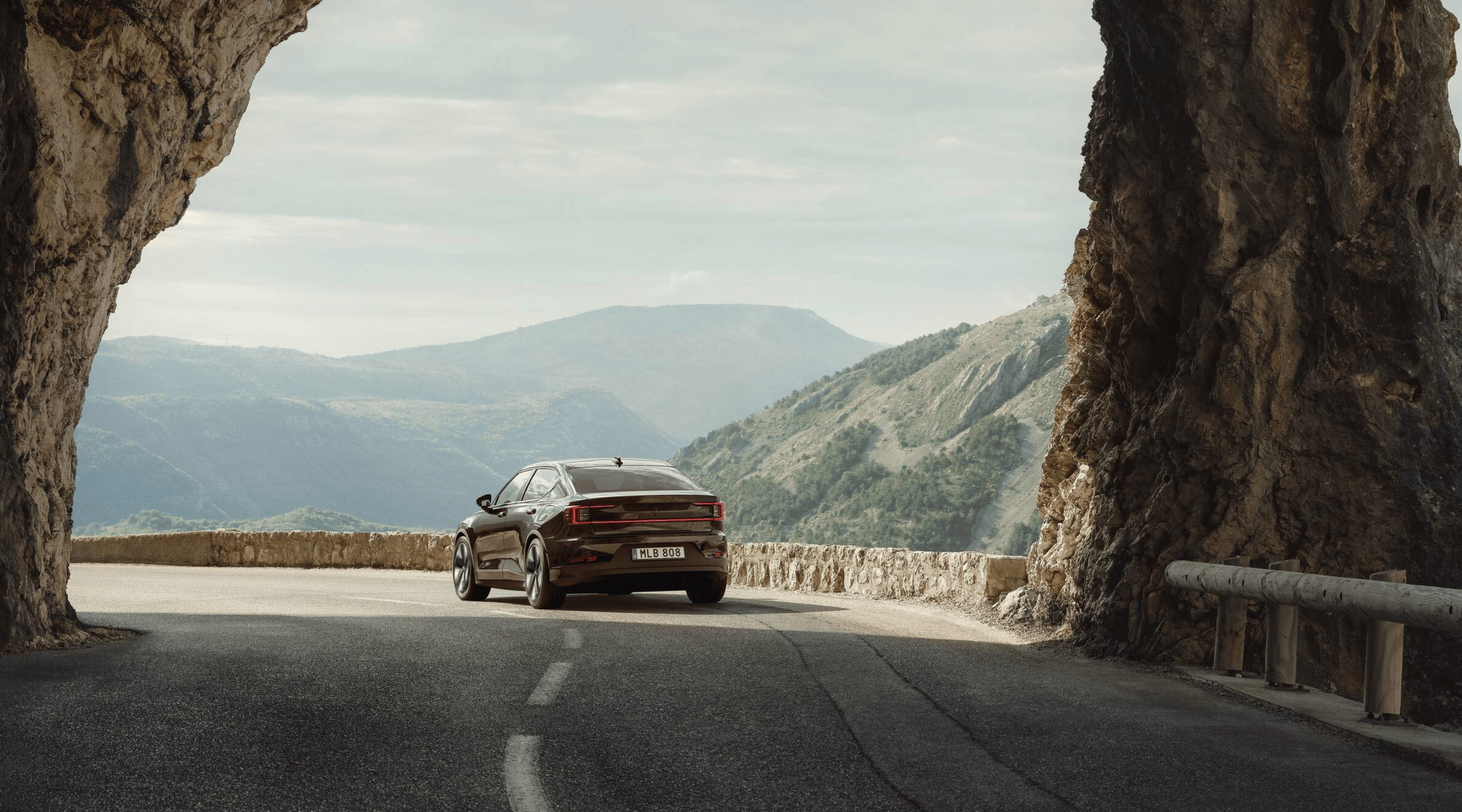 Polestar 2 driving away from an arched rock formation on a highway in a hilly area.