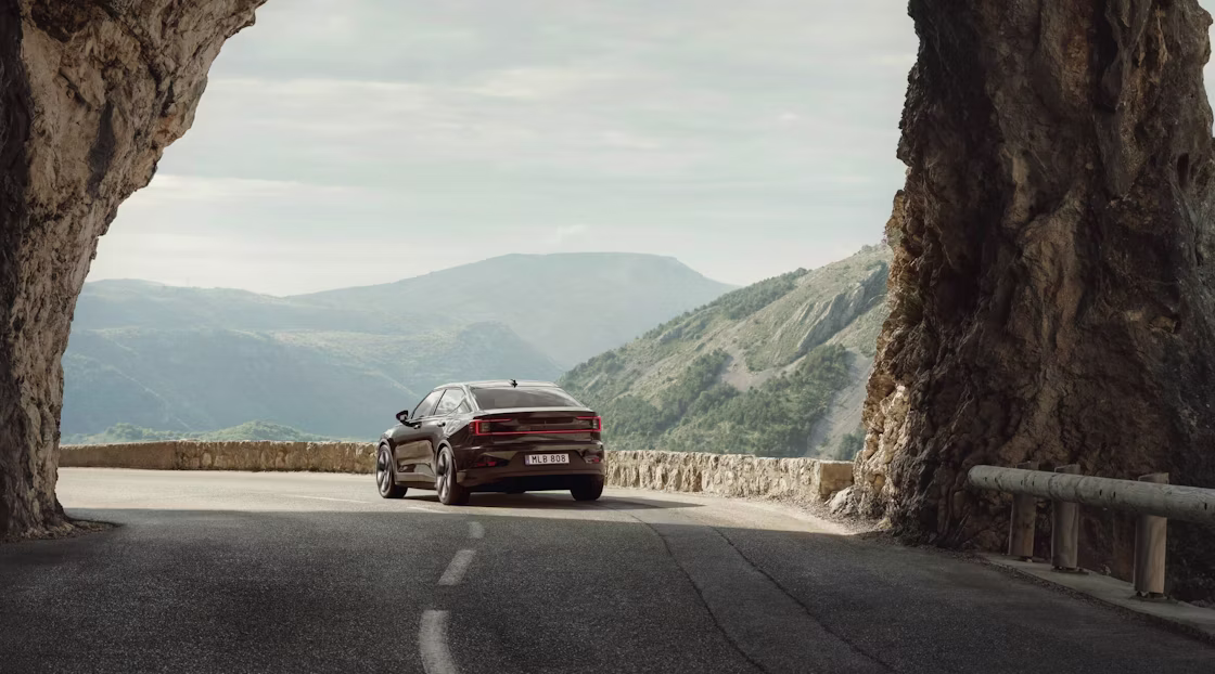 Polestar 2 driving away from an arched rock formation on a highway in a hilly area.