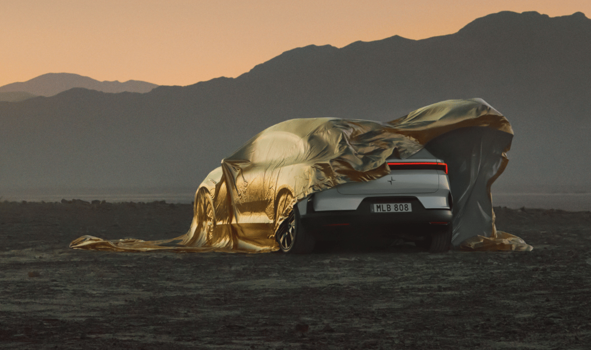 Polestar 4 coupé partially covered by a gold sheet in a desert at sunset