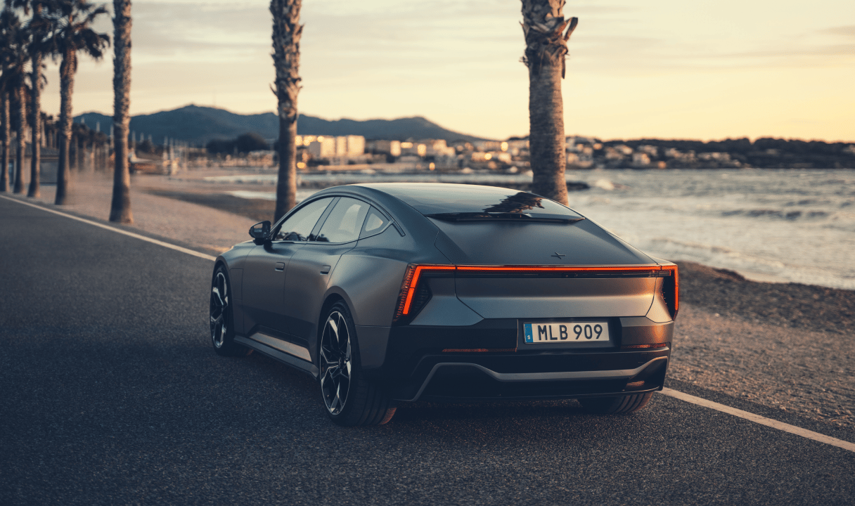 Polestar 5 driving by a waterfront road at sunset
