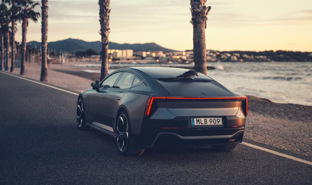 Polestar 5 driving by a waterfront road at sunset