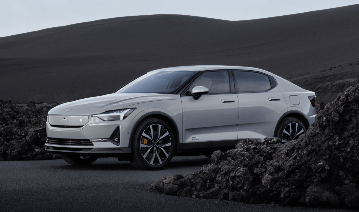 Polestar 2 parked on a road beside dark rocks and sand dunes