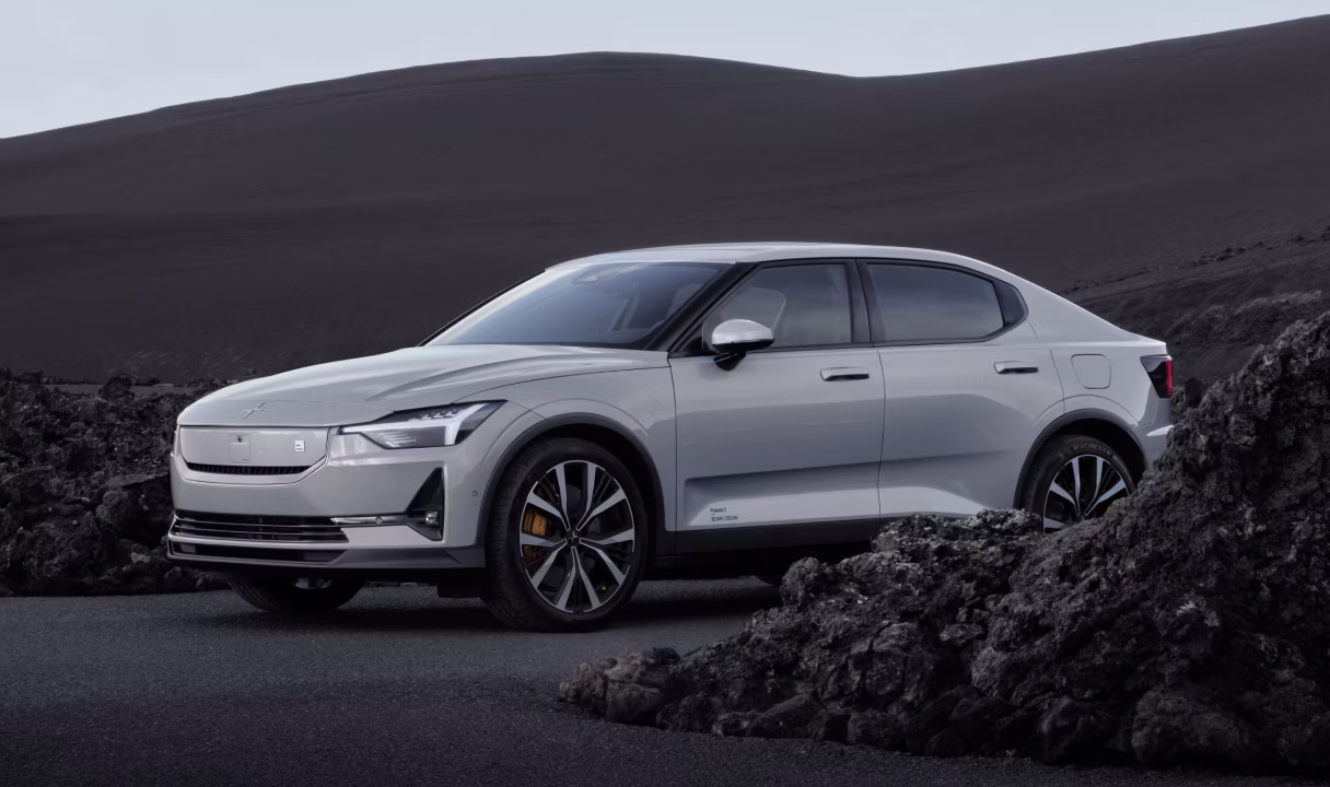 Polestar 2 parked on a road beside dark rocks and sand dunes