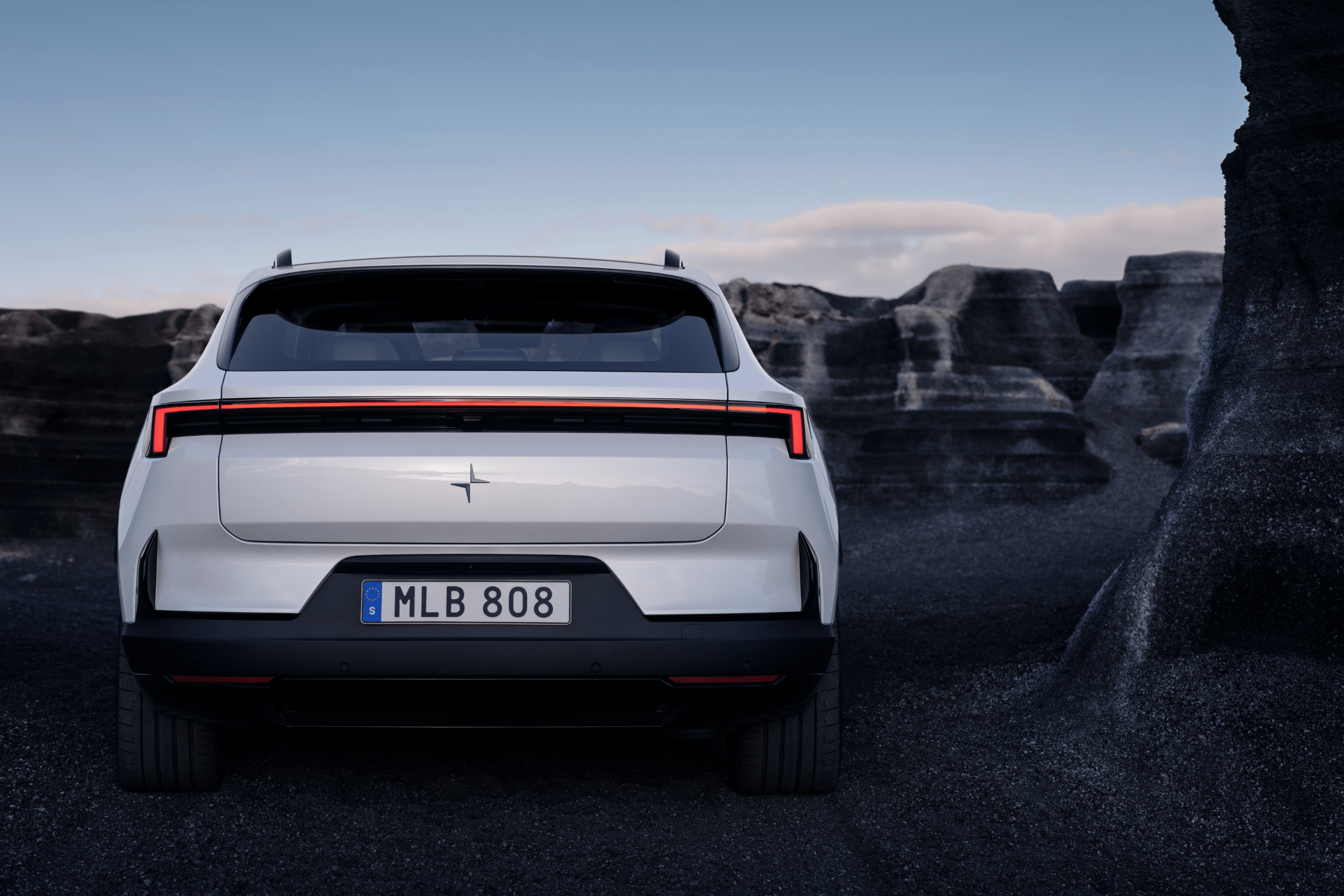 Heckansicht eines weissen Polestar 4 SUV an einer Küstenlandschaft mit Felsen am Meer.