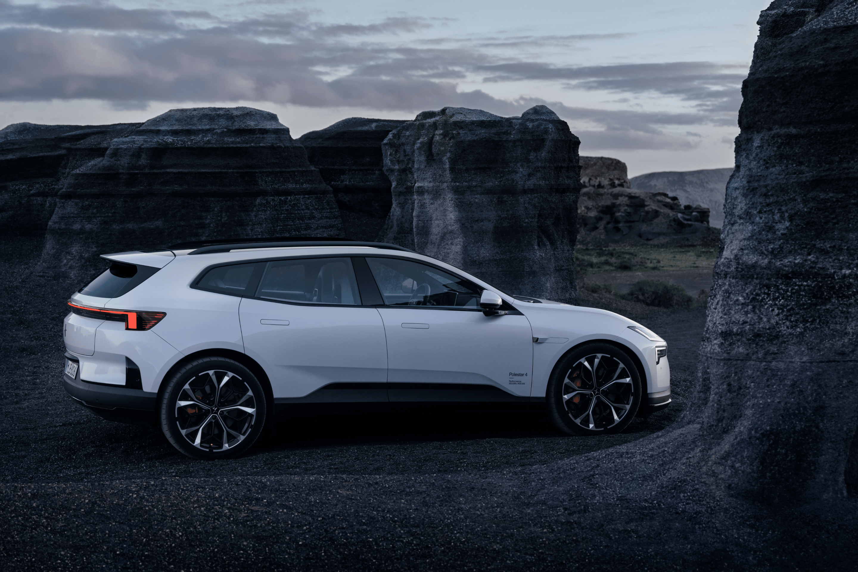 Side view of a white Polestar 4 SUV standing near grey seaside cliffs.