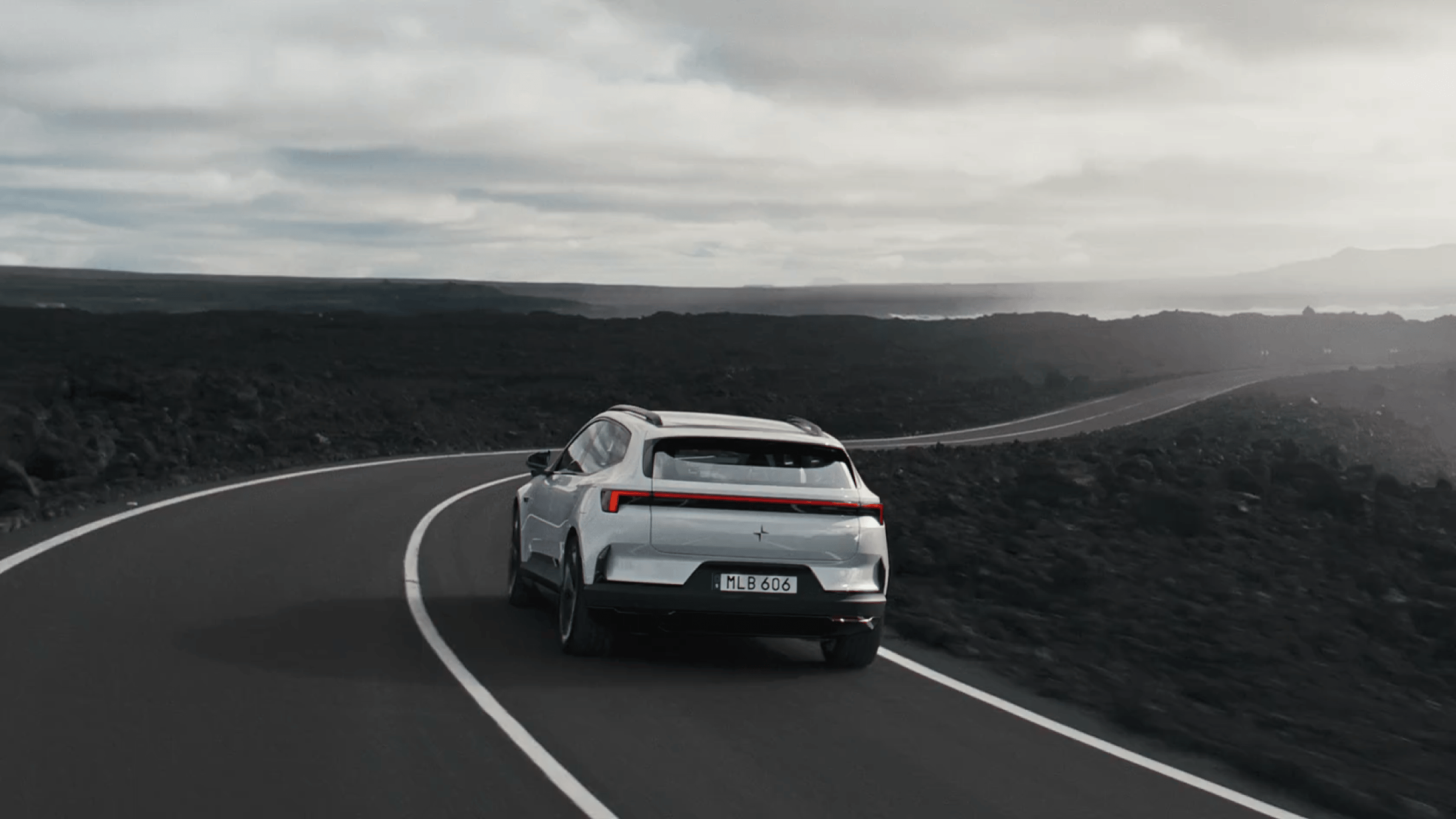 A white Polestar 4 SUV driving on a highway by the ocean and sea cliffs.