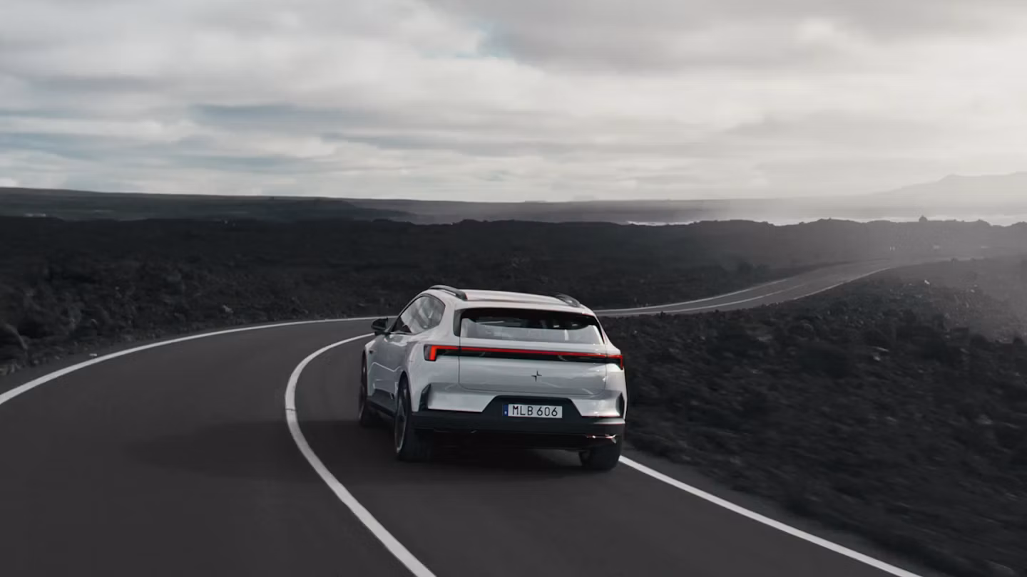 A white Polestar 4 SUV driving on a highway by the ocean and sea cliffs.