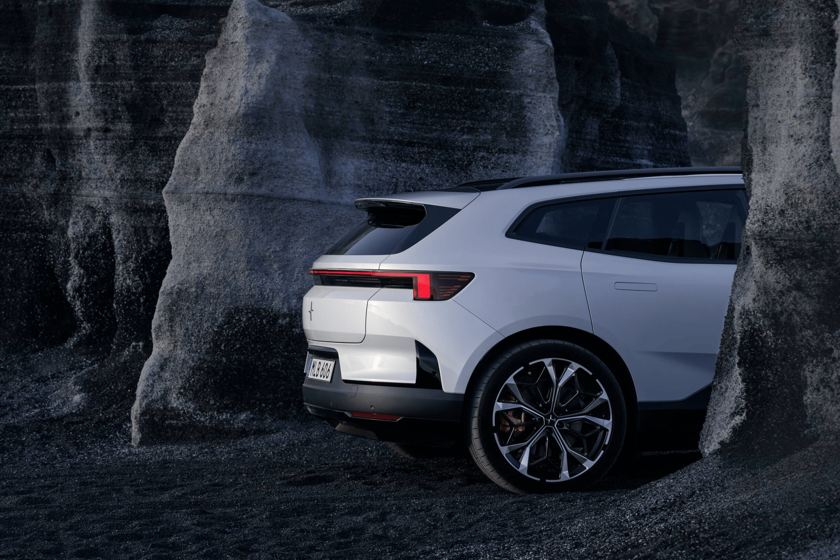 Rear side portion of a white Polestar 4 SUV standing between a grey rock formation.