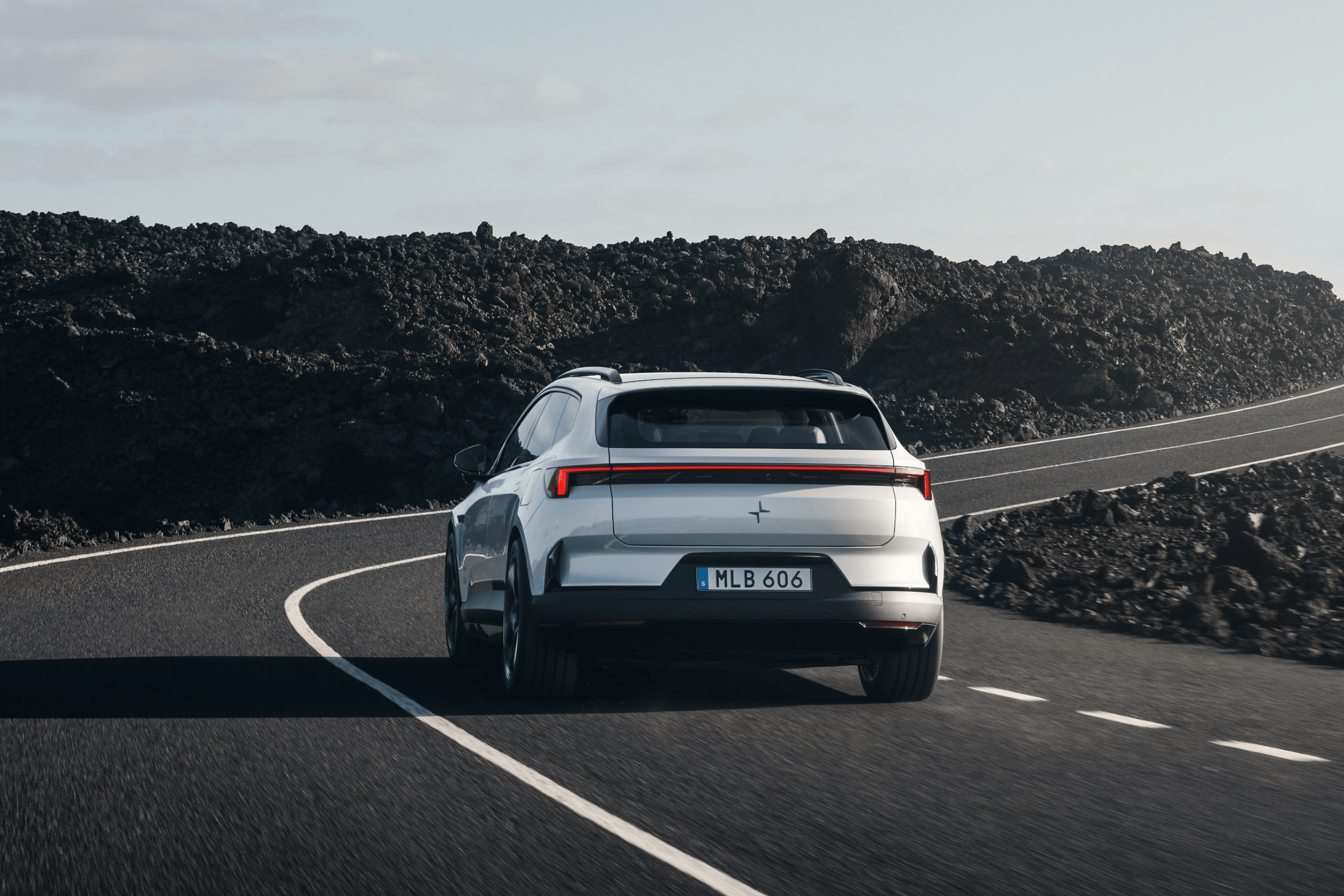 Rear profile view of a white Polestar 4 SUV driving on a road surrounded by rocky terrain.