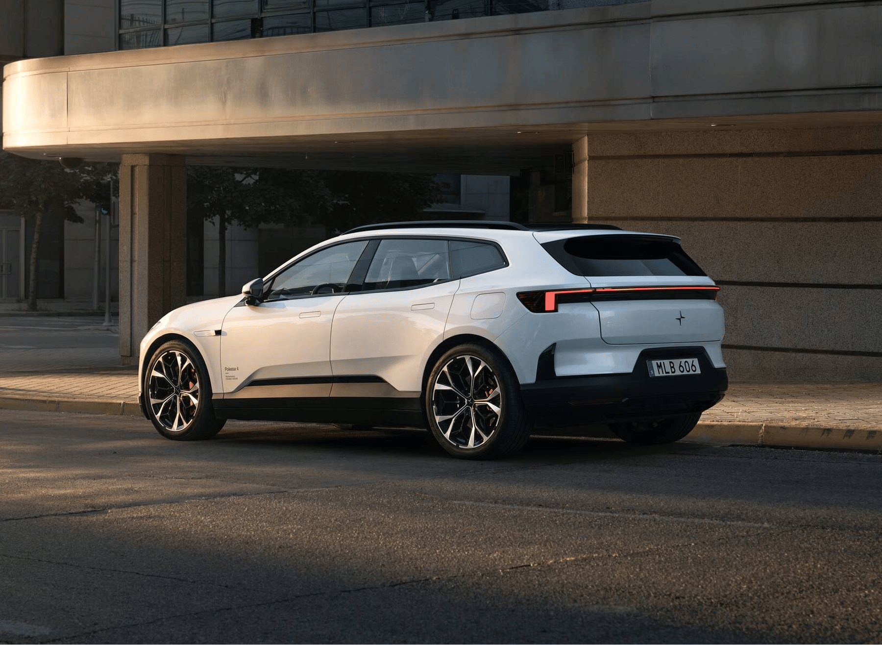 Vit Polestar 4 SUV sedd från sidan parkerad utanför en betongbyggnad.